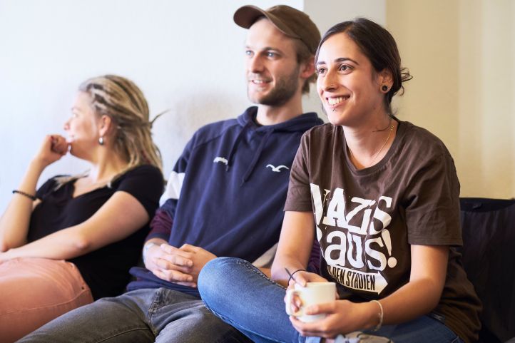 Mehrere Jugendliche zwei junge Frauen und ein junger Mann nehmen an einem Workshop Seminar teil und lächeln