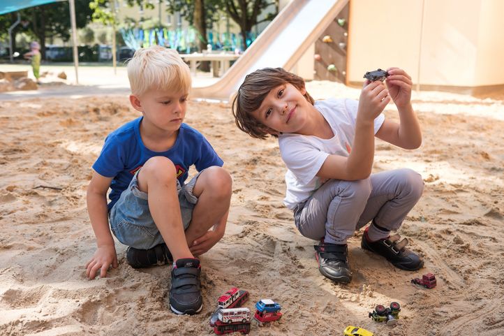 zwei Kinder sitzen im Sandkasten und lachen in die Kamera