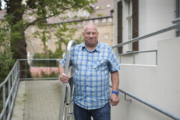 Ein Mann hat sich eine Leiter über die Schulter gelegt und grinst