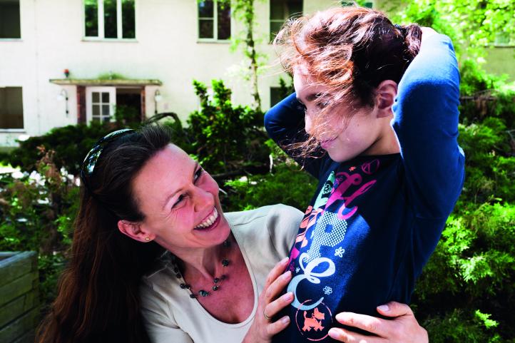 Eine lachende Frau schaut ein Mädchen an, das sie sich Haare bindet