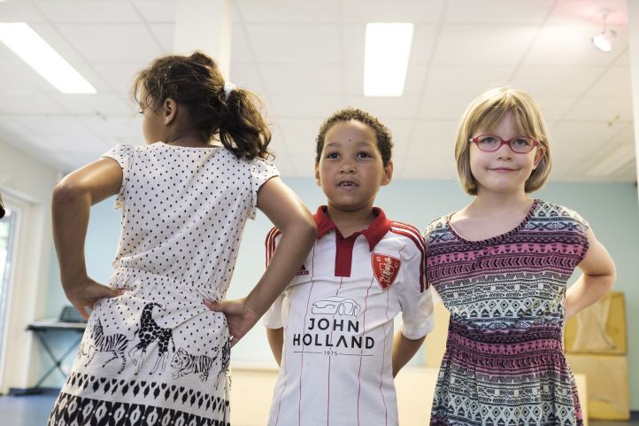 Das Bild zeigt drei Kinder, links ein Mädchen mit dem Rücken zu Kamera, daneben ein Junge und ganz rechts wieder ein Mädchen.
