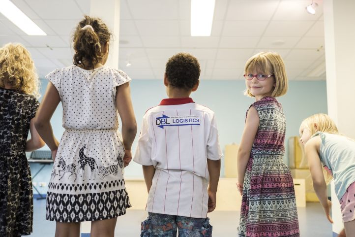 Kinder drehen dem Betrachter den Rücken zu, nur ein Mädchen schaut lächelnd in die Kamera
