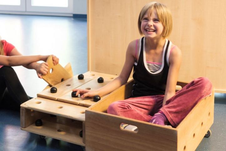 Zwei lachende Mädchen spielen mit einem selbstgebauten Holzwagen, in dem eine von ihnen sitzt