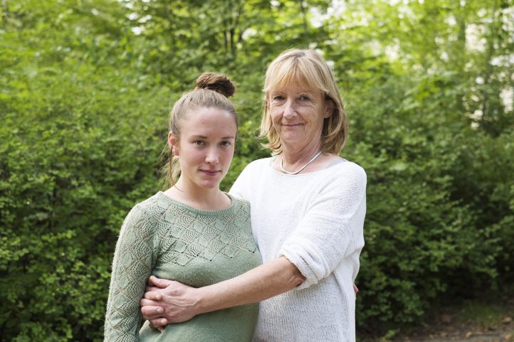 Eine Frau im mittleren Alter hält eine junge Frau im Arm und beide lächeln in die Kamera