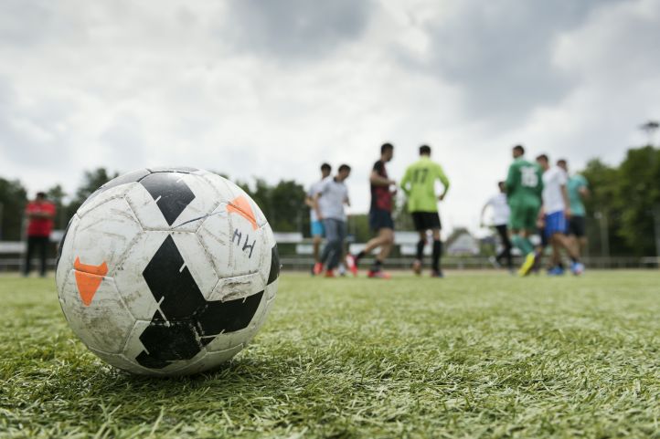 Ein Fußball im Vordergrund, unscharf im Hintergrund Fußball spielende Menschen