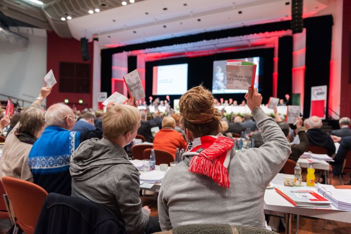 Abstimmung im Konferenzsaal, Im Vordergrund zwei junge Teilnehmende, die ihre Stimmkarte hochhalten.