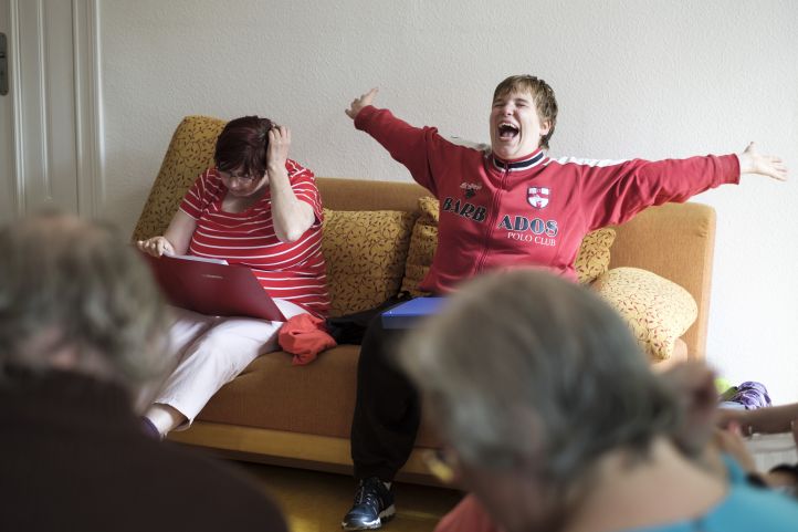 Eine lachende Frau sitzt mit ausgebreiteten Armen neben einer anderen Frau auf dem Sofa