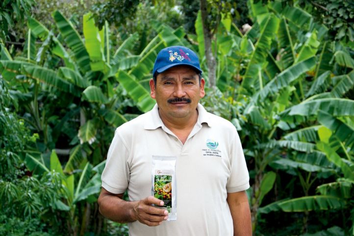 Ein Kaffeebauer steht vor einer Plantage und lächelt in die Kamera
