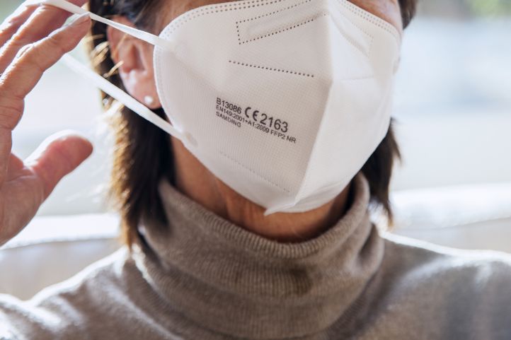 Eine ältere Frau Rentnerin Seniorin setzt sich eine FFP2-Maske auf