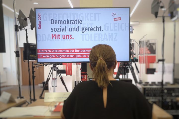 Blick auf das Motto der Buko 2021 auf einem Monitor, davor sitzt eine Frau in Rückensansicht