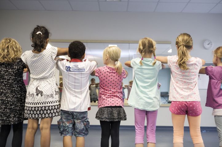 Kinder stehen mit dem Rücken zum Betrachter in einer Reihe. 