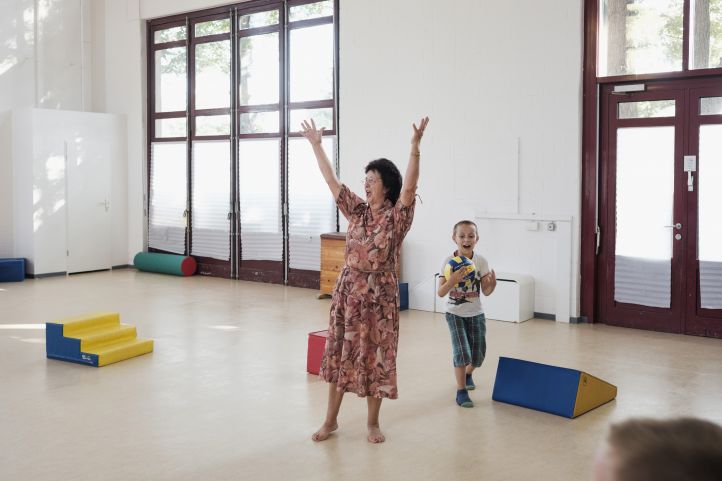 Eine alte Frau Seniorin jubelt mit einem Kind Jungen und einem Ball in einer Turnhalle